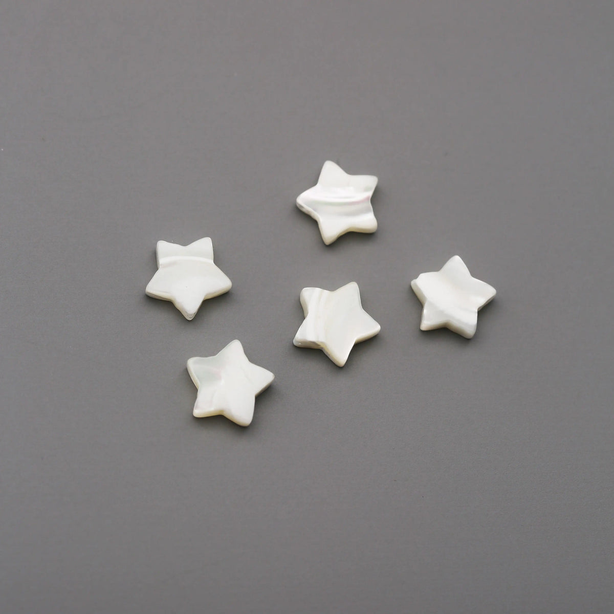Five 10mm star-shaped shell beads from Printable Heaven are arranged in a semi-circle on a smooth, gray surface.