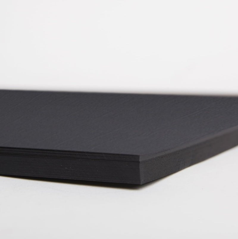 A close-up of the corner of a Printable Heaven A4 Textured Premium Cardstock - Capsule Black (PMA 1641502) sheet, showcasing its canvas texture against a plain white background.
