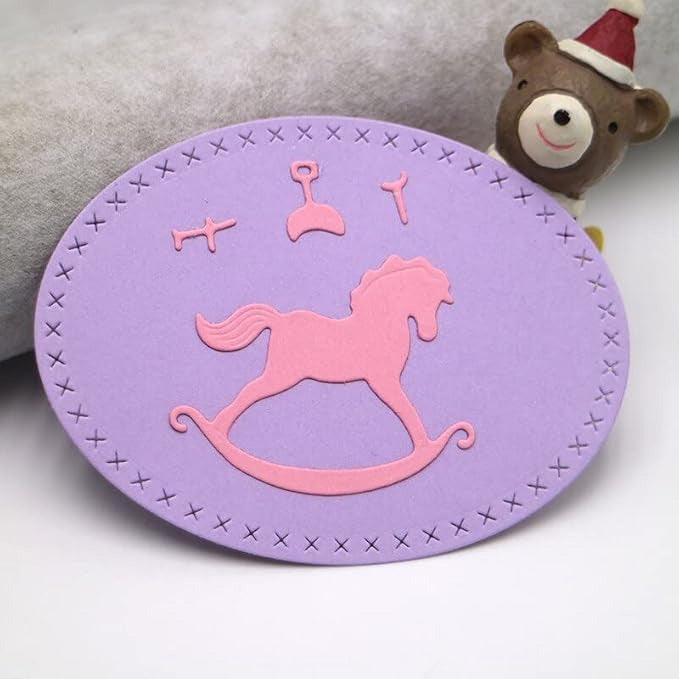 A purple oval card with a pink rocking horse and baby items design, featuring a stitched border—ideal for use with the Printable Heaven Rocking Horse Cutting Die (4 pcs) (A108) or other die-cutting machines to create charming baby shower decorations; a small teddy bear toy with a red hat appears in the background.