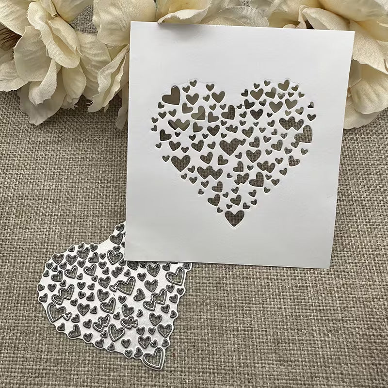 A heart-shaped stencil featuring an array of small heart cut-outs rests on burlap, accompanied by the Printable Heaven Filigree Heart Cutting Die (1 PC) (SP058) and cream flowers—ideal accents for your card-making projects.