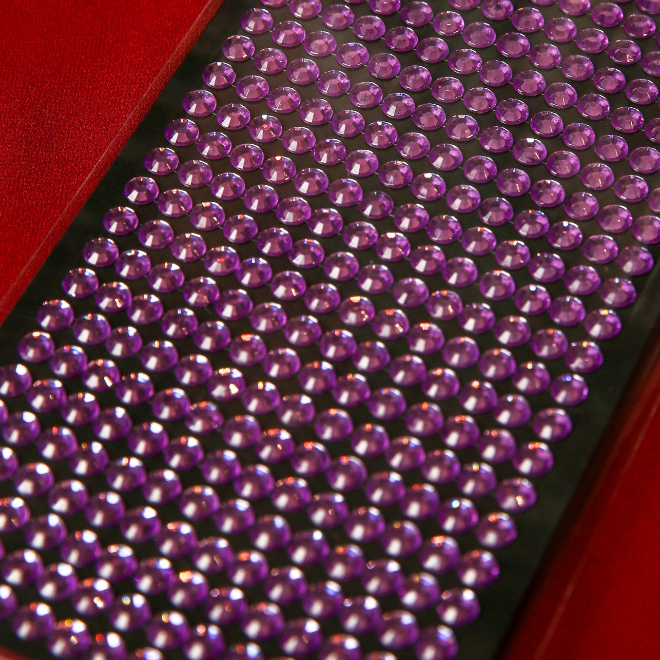 Printable Heaven's 6mm Purple Crystal Sticky Gems, featuring small round self-adhesive jewels with a faceted surface for sparkle, are neatly arranged on a black tray against a red background.