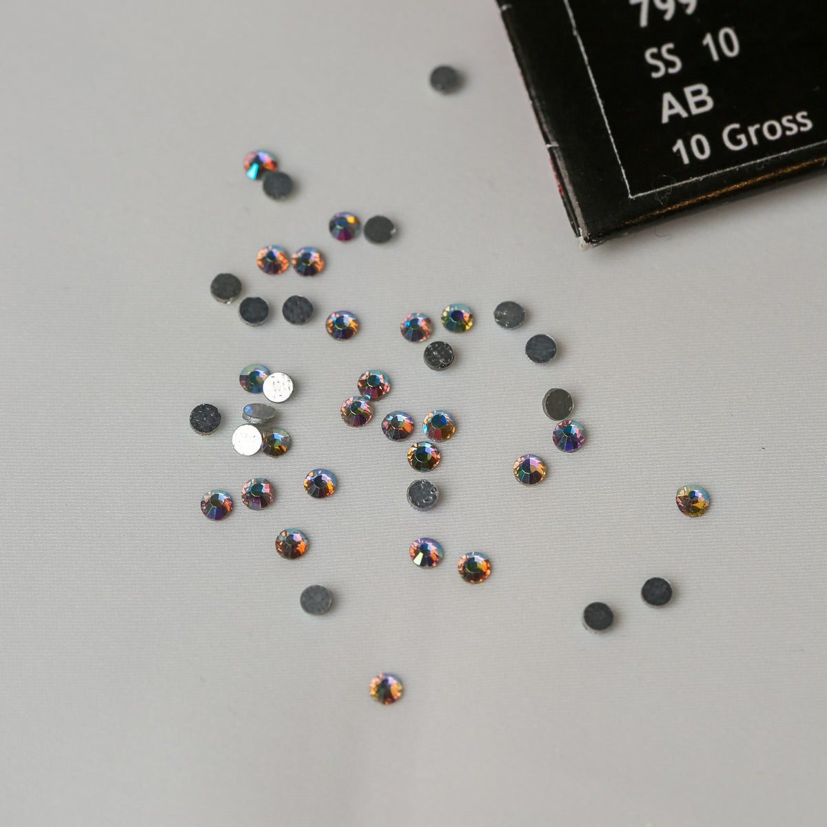 SS10 Hot Fix Silver Foiled AB Crystals scattered on a gray surface next to a partial Printable Heaven product label.