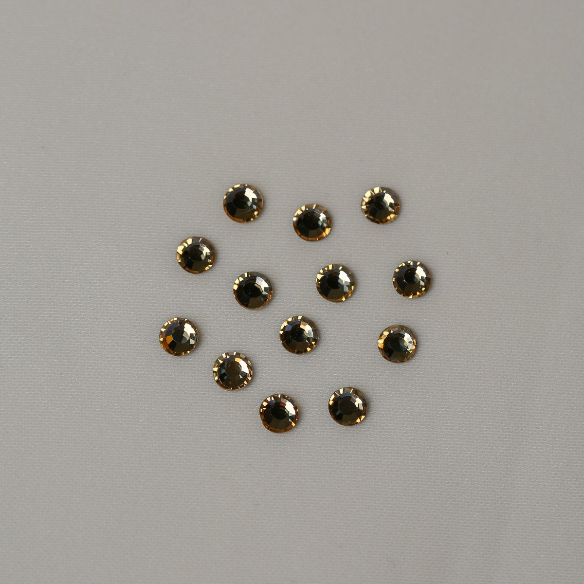 Eleven small, round, golden-brown faceted SS16 Non-Hot Fix Silver Foiled Crystals in Golden Shadow arranged in a cluster on a light gray surface.
