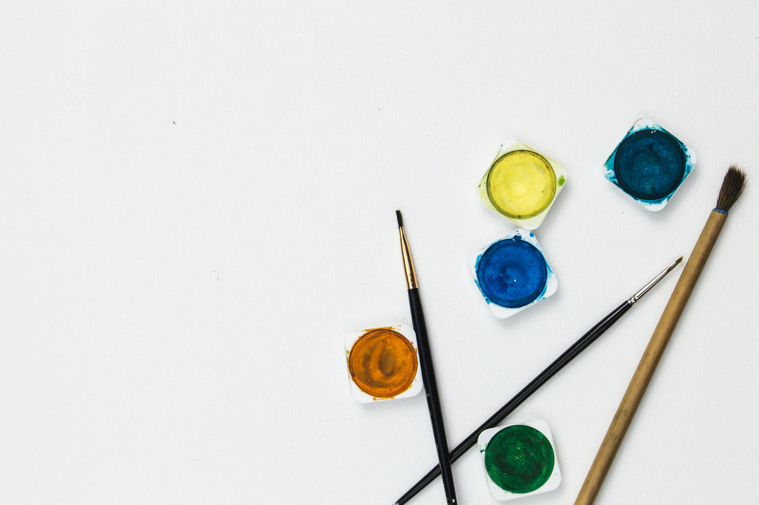 Green, blue, yellow and gold paint next to three thin paintbrushes.