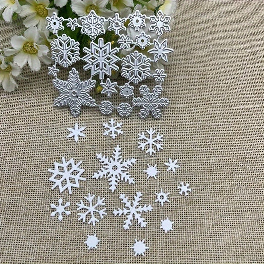 The Winter Snowflake Cutting Die Set (20 PCS) (SP046) by Printable Heaven features intricate silver snowflake-shaped metal dies, perfect for Christmas crafts or winter-themed projects, beautifully displayed on a beige textured fabric with delicate white flowers in the corner.