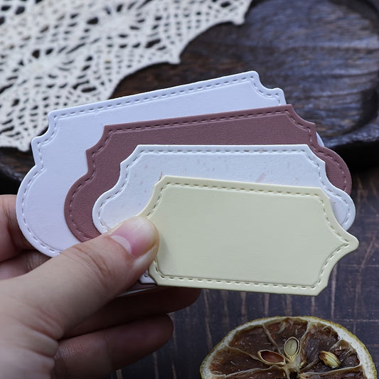 A hand displays four beautifully shaped tags in cream, white, maroon, and light gray, each precision-cut using the Stitched Edge Nesting Frame Dies – Set of 4 (D124) by Printable Heaven for crisp, decorative edges. In the background, a brown dried citrus slice and a crochet doily add a charming touch—perfect inspiration for card making projects.