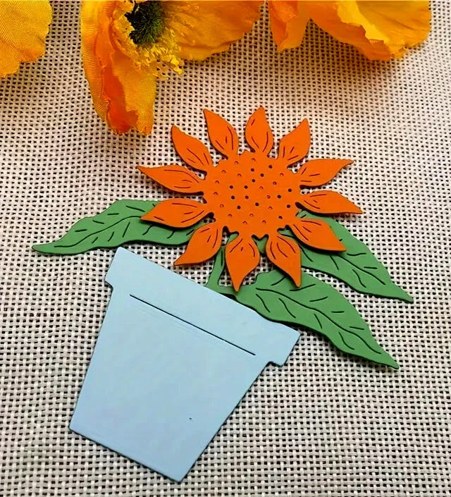 Create beautiful sunflower-themed crafts with the Printable Heaven Sunflower & Pot Plant Cutting Die (3 PCS) (F036). Featuring an orange sunflower with green leaves in a light blue pot, this cutting die set is perfect for paper craft enthusiasts and anyone who enjoys adding cheerful botanical touches to their décor. Display your finished project on a textured beige surface alongside yellow fabric flowers for added charm.