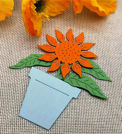 Create beautiful sunflower-themed crafts with the Printable Heaven Sunflower & Pot Plant Cutting Die (3 PCS) (F036). Featuring an orange sunflower with green leaves in a light blue pot, this cutting die set is perfect for paper craft enthusiasts and anyone who enjoys adding cheerful botanical touches to their décor. Display your finished project on a textured beige surface alongside yellow fabric flowers for added charm.