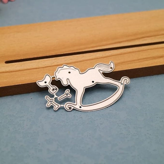 A Printable Heaven Rocking Horse Cutting Die set (4 pcs) (A108), ideal for use with die-cutting machines, is displayed on a blue surface beside a wooden piece featuring a long slot.