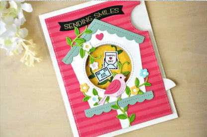 Crafted with the Printable Heaven Large Cuckoo Clock Cutting Die (13 PCS) (A030), this handmade greeting card showcases a delightful chalet-inspired birdhouse, a pink bird, flowers, and leaves. The card features “SENDING SMILES” and “HAPPY DAY” sentiments on a pink striped background, finished with delicate white flowers in the top left corner.
