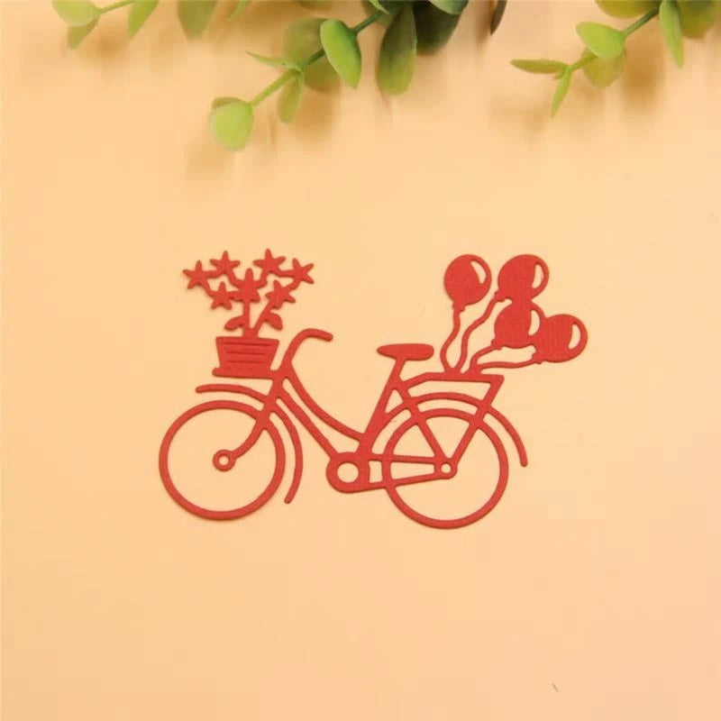 A charming scene showcasing the Printable Heaven Bicycle with Balloons & Gifts Cutting Die (1 PC) (D104)—a red outline of a bicycle adorned with a potted plant at the front and balloons at the back, set against a light background with green leaves overhead—perfect for adding delightful embellishments to your paper crafting projects.
