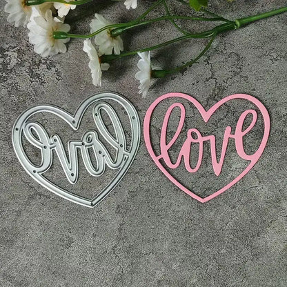 Two heart-shaped cutouts—one silver and one pink—rest on a gray surface, each featuring the word “love” in elegant cursive, intricately crafted with the Printable Heaven Love Heart Cutting Die (1 PC) (W094). Delicate white flowers with green stems are arranged above the cutouts, making this setup perfect for wedding crafts or romantic décor.
