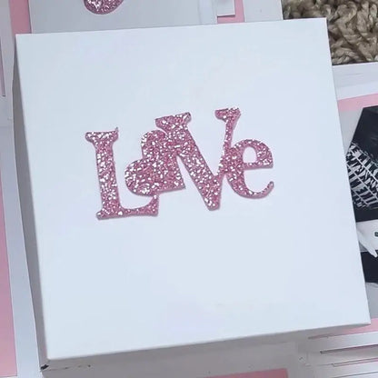 A white LOVE Sentiment Cutting Die (1 PC) by Printable Heaven, featuring the word “Love” in pink glittery letters, is perfect for storing handmade cards or adding a charming touch to your papercraft projects.