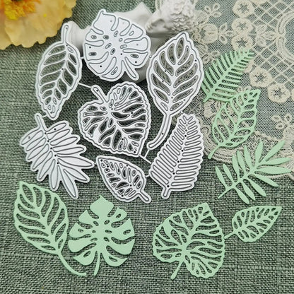 Printable Heaven’s Tropical Leaves Cutting Die Set (7 PCS) (L011) and their delicate light green paper cutouts are beautifully arranged on a textured green fabric, accented by lace and a yellow flower in the background. These metal cutting dies are perfect for botanical paper crafts and card making, adding a lush, natural touch to your creative projects.