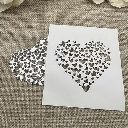A white stencil featuring a heart shape composed of smaller hearts rests on burlap beside a matching cut-out pattern, both demonstrating the intricate detail achievable with the Printable Heaven Filigree Heart Cutting Die (1 PC) (SP058)—ideal for card making. Cream flowers are partially visible at the top.