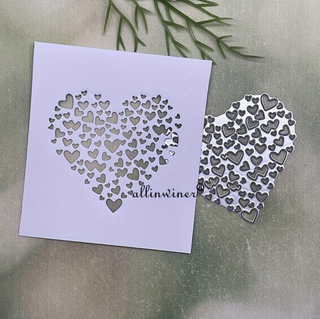 The Filigree Heart Cutting Die (1 PC) (SP058) from Printable Heaven is showcased alongside a white card, both adorned with an intricate large heart composed of multiple smaller heart cutouts. Set against a green, nature-inspired background, this design is ideal for creating elegant handmade cards.