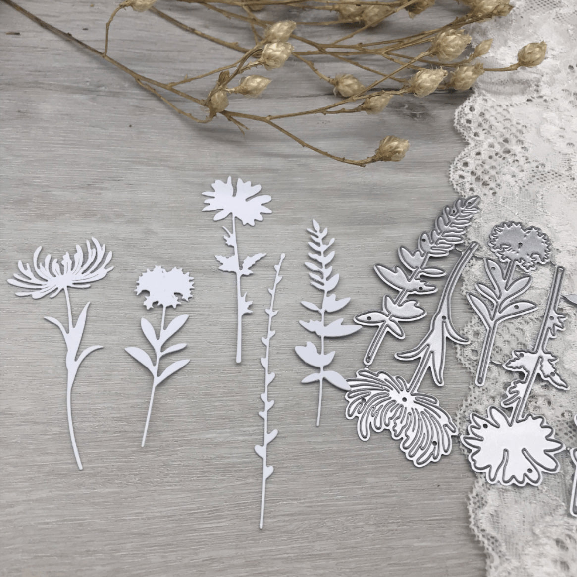 The Printable Heaven Wildflower Meadow Cutting Die Set (4 PCS) (DJ026) and white paper flower cutouts are arranged on a light wooden surface, with dried flowers and lace in the background.