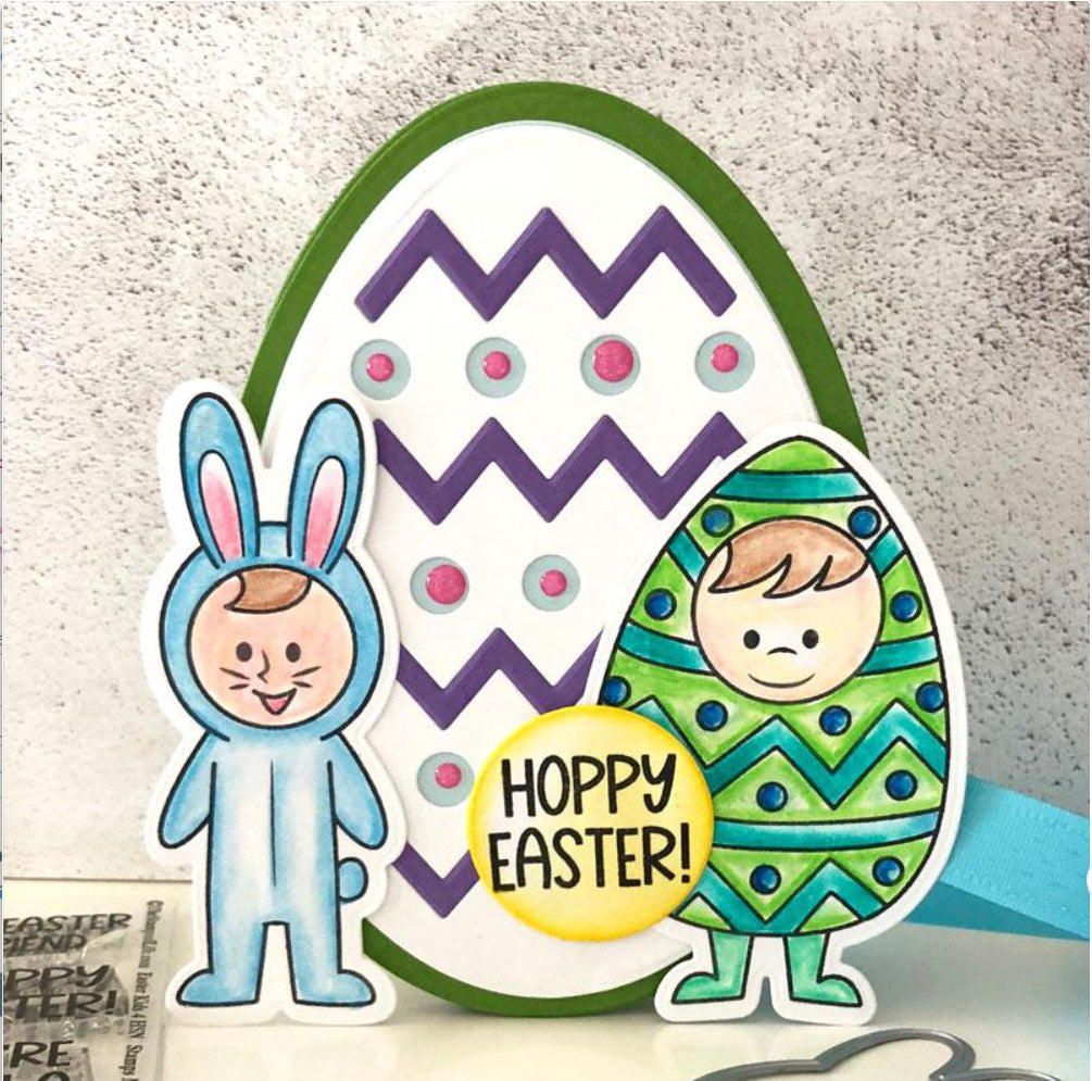 Created with the Printable Heaven Easter Egg Metal Cutting Die (1PC) (A124), this handmade Easter card is perfect for Easter card making or scrapbooking. The design showcases a large, intricately decorated egg, featuring a child in a blue bunny costume and another dressed as an egg. A bright yellow circle adds cheer with playful “Hoppy Easter!” text.