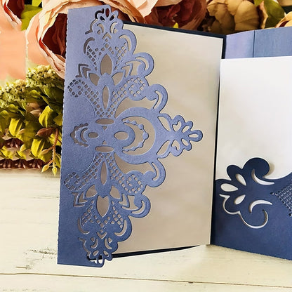 A blue greeting card featuring an intricate laser-cut floral design on the front, crafted with the Printable Heaven Filigree Corner Cutting Die (1 PC) (B007), is displayed open on a light wooden surface with flowers in the background—an ideal addition to your next papercrafting project.