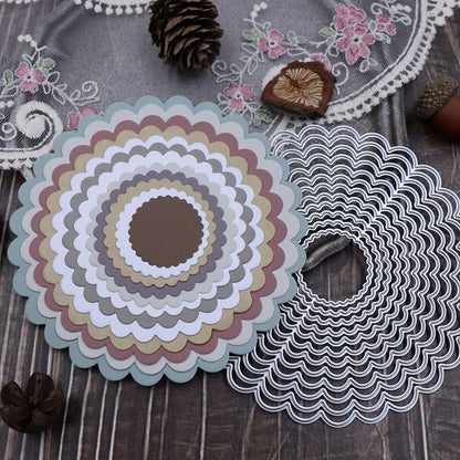 A collection of muted paper circles, cut with the Printable Heaven 12-Piece Scalloped Circle Cutting Die Set (D140), is artfully arranged next to nested black and white die-cut circles on a wooden surface—an inspiring setup for cardmaking or scrapbooking. Pinecones and floral embroidered lace in the background add a quaint, charming touch.