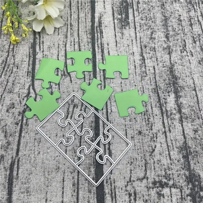 Six green jigsaw puzzle pieces, created with the Printable Heaven Jigsaw Puzzle Cutting Die (6 PCS) (T071), along with an empty white puzzle piece frame, are arranged on a gray textured surface, accented by white flowers in the top left corner—an ideal setup for cardmaking or scrapbooking projects.