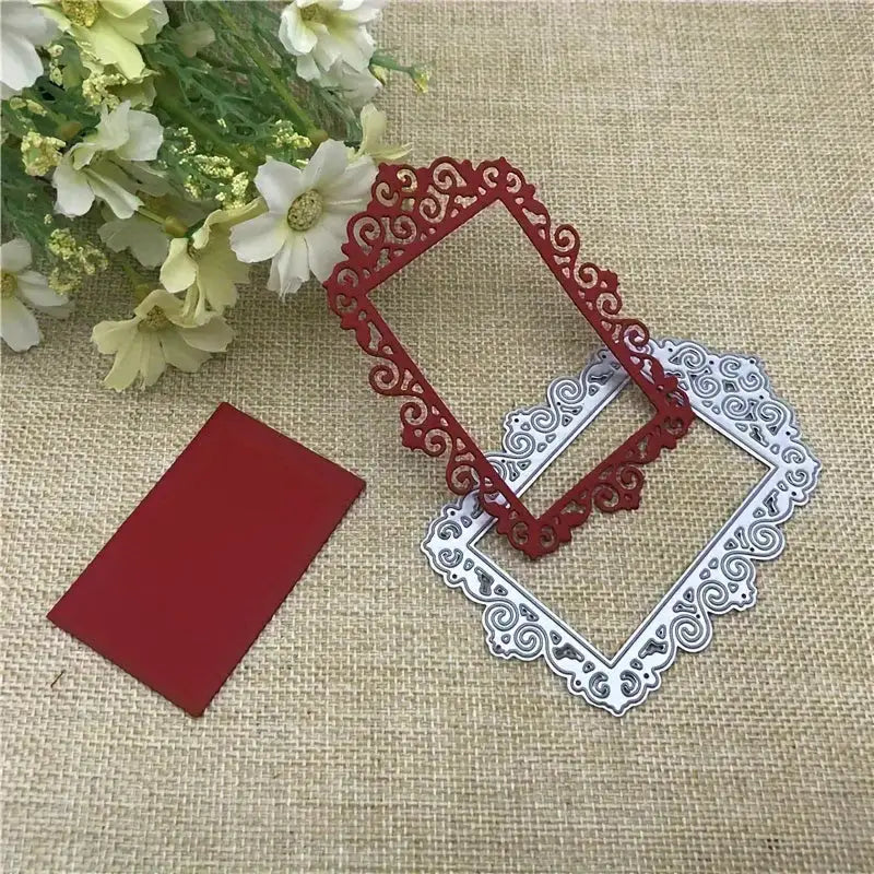 A red rectangular metal cutout created with the Ornate Decorative Frame Cutting Die (1 PC) (T048) from Printable Heaven, a matching silver decorative frame die, and a solid red rectangle are displayed on burlap next to white flowers with green leaves.