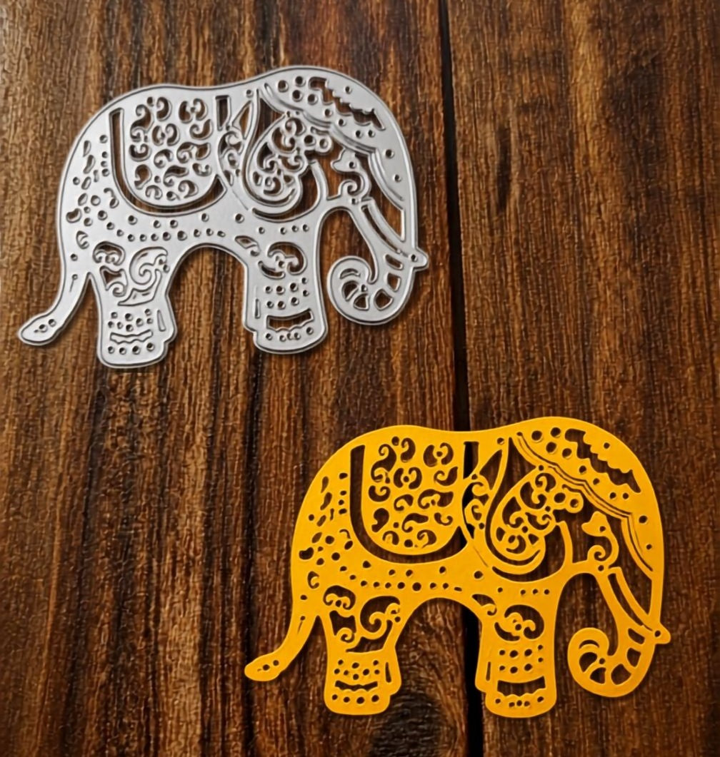 Two intricately cut elephant-shaped decorations—one silver and one yellow—created with the Printable Heaven Elephant Filigree Cutting Die (1 pc) (A070Q), lie on a wooden surface.