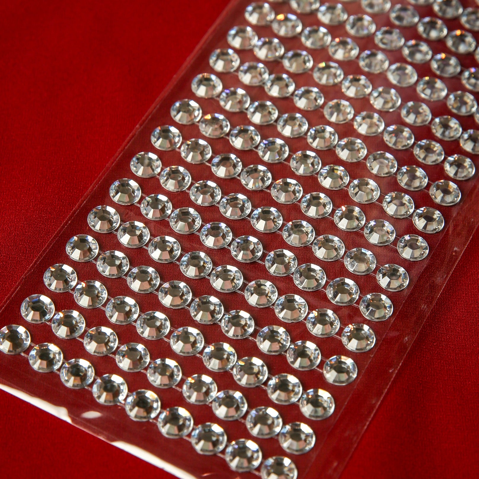 A sheet of Printable Heaven 10mm Silver Crystal Adhesive Jewels—small, round, and clear—arranged in neat rows on red fabric, ideal for embellishing your crafts or decor projects.