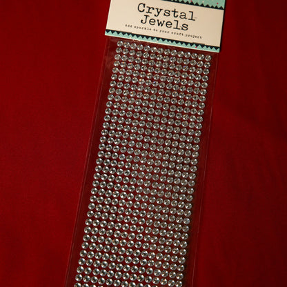 A pack of Printable Heaven 6mm Silver Crystal Adhesive Jewels arranged on a clear sheet, ideal for adding sparkle to crafts, scrapbook embellishments, or Christmas cards, shown on a red background.