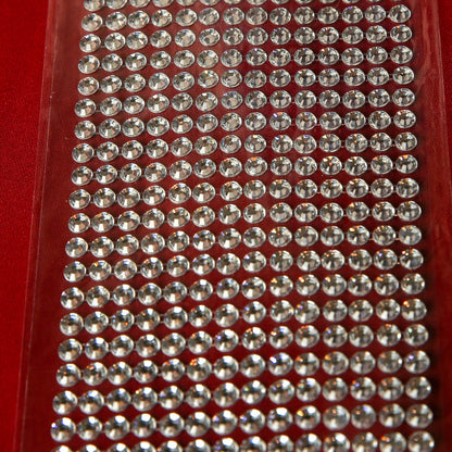 A close-up of Printable Heaven’s 6mm Silver Crystal Adhesive Jewels—small round stickers arranged in neat rows on a clear backing, ideal for scrapbooking or embellishments, shown against a red background.