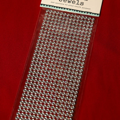 A sheet of Printable Heaven 6mm Silver Crystal Adhesive Jewels is displayed on a red surface. The packaging reads "Jewels," with gems arranged in neat rows—ideal for Christmas cards or scrapbook embellishments.
