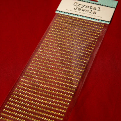 A pack of Printable Heaven 3mm Gold Crystal Adhesive Jewels is displayed on a red background—ideal for adding festive sparkle to Christmas cards.