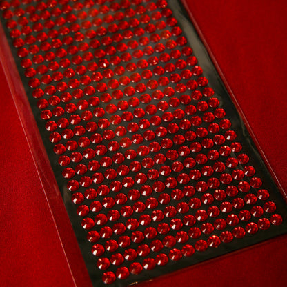 A sheet of Printable Heaven 6mm Red Crystal Sticky Gems, small round self-adhesive jewels arranged on black backing, ideal for crafts and displayed on a red surface.
