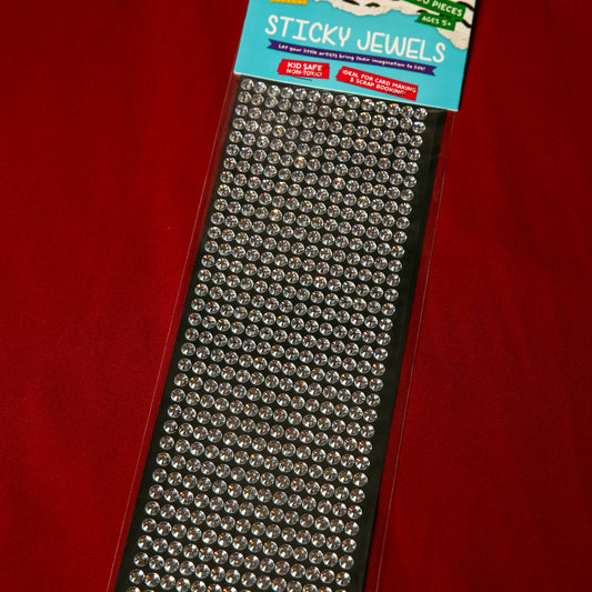 A pack of Printable Heaven 6mm Silver Crystal Sticky Gems—small, round, self-adhesive jewels on black backing—displayed on a red surface. Ideal for adding sparkle to craft projects.
