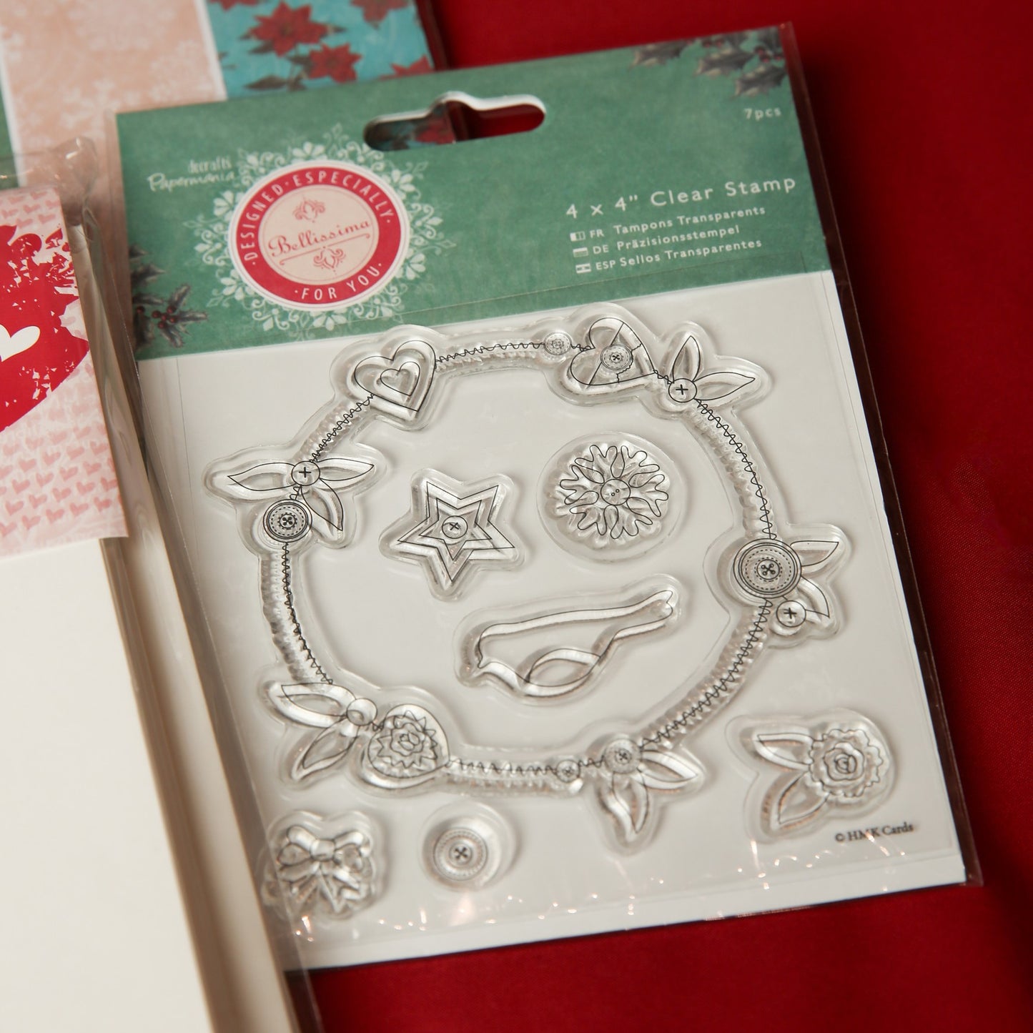 The Printable Heaven Bellisima Christmas Papercrafting Kit includes clear stamps with flowers, hearts, a star, a circle, and leaves—ideal for Christmas cards, scrapbooking, or crafts. The package is shown partly on a red surface.