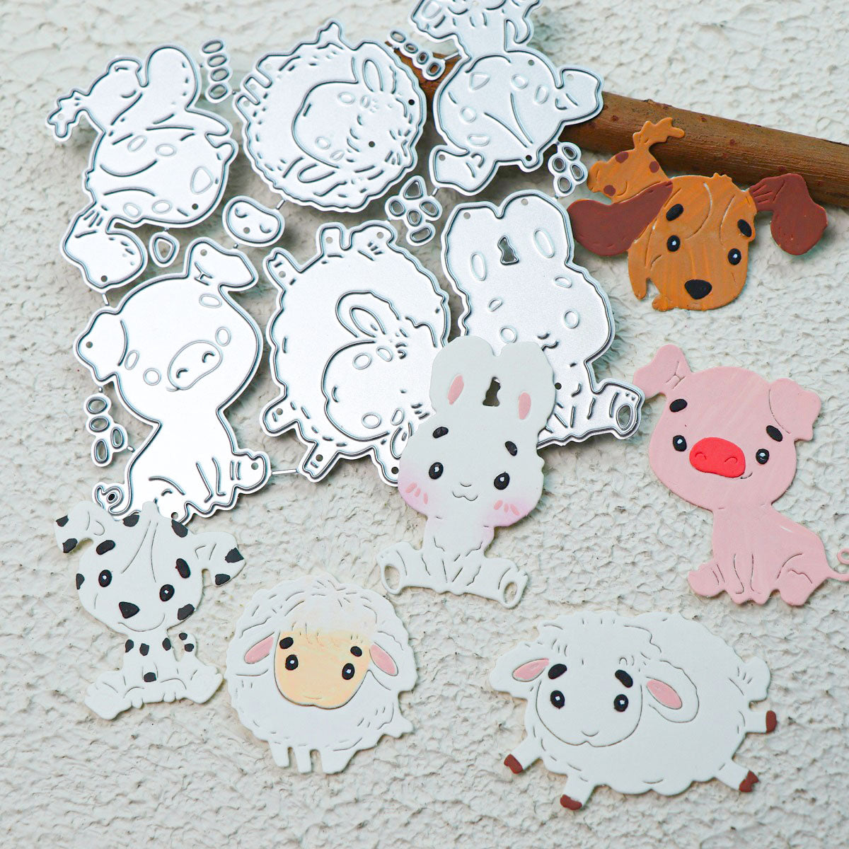 Metal cutting dies and pastel paper cutouts of adorable barnyard animals, crafted with the Cute Kawaii Animal Character Cutting Die Set (6 pcs) (A057) from Printable Heaven, are arranged on a textured white background. Ideal for paper crafting projects, the charming dog, pig, lamb, and cow feature expressive kawaii faces that bring a delightful touch to any creation.