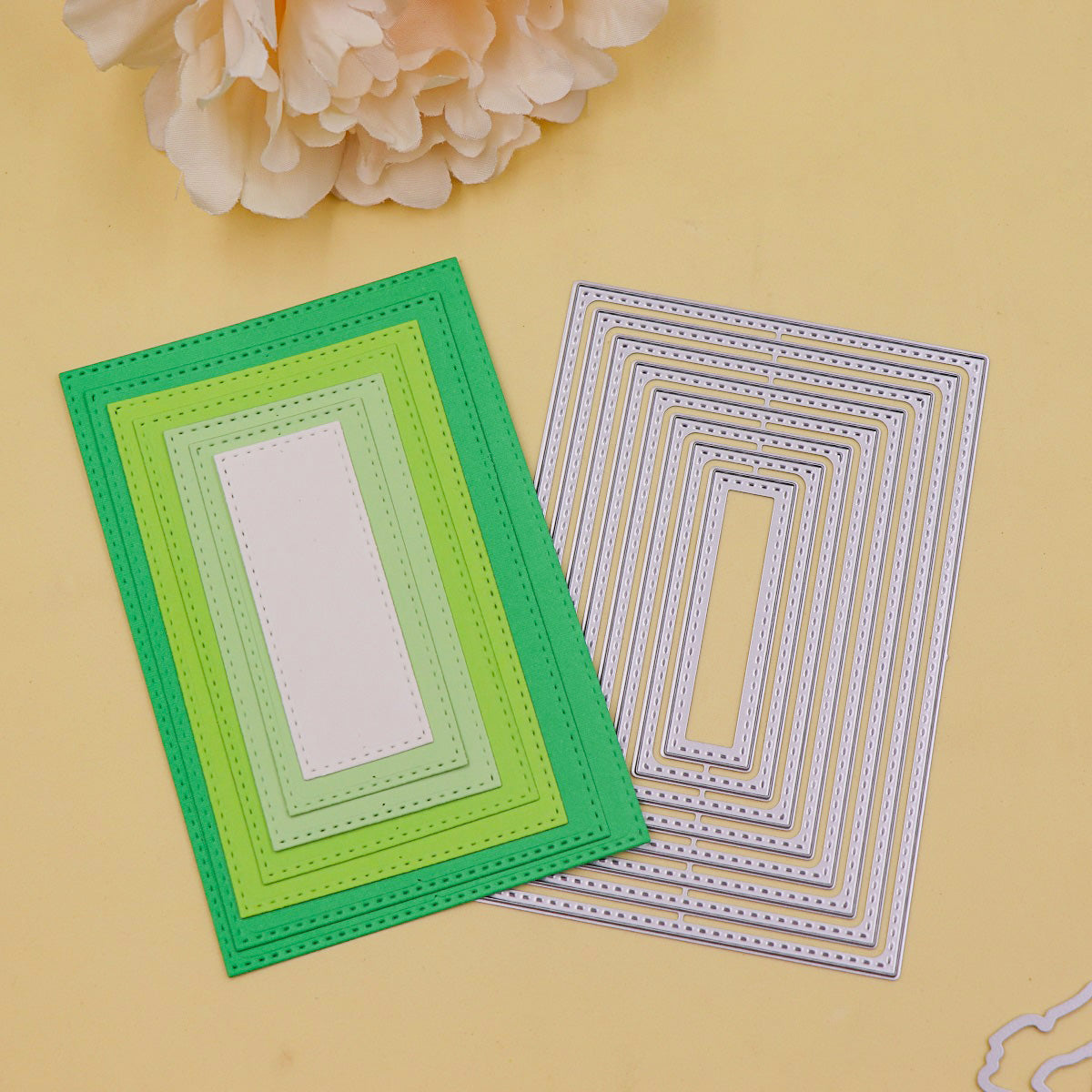 A set of Printable Heaven Stitched Edge Nesting Rectangle Cutting Dies (8 PCS) (SP097) is arranged on a yellow surface, each die in a silver metal finish with stitched-edge detailing perfect for card making; a large pale flower is partially visible in the top left corner.