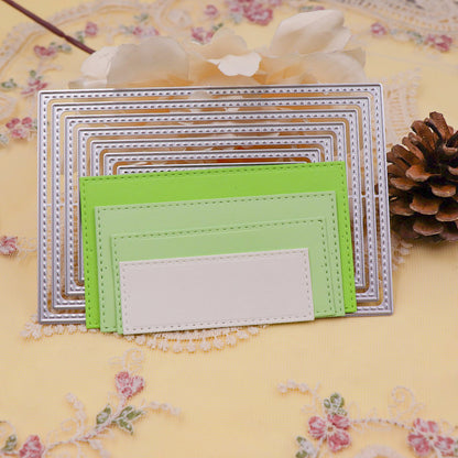 Here’s the revised sentence using your product data: Printable Heaven’s Stitched Edge Nesting Rectangle Cutting Dies (8 PCS) (SP097) are used to create layered metal and colored die-cut frames with detailed stitched edges, beautifully arranged on embroidered yellow fabric—ideal for card making projects. A white flower and pinecone in the background add a charming finishing touch.