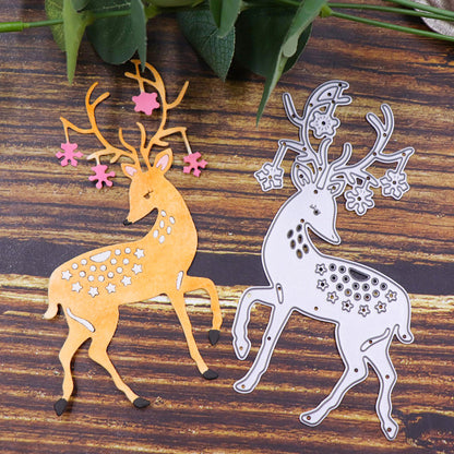 Two decorative reindeer stag cutouts created with the Majestic Reindeer Stag Cutting Die (1 PC) (SP013) by Printable Heaven showcase one design in yellow with pink antlers and star accents, and another in silver with intricate embossed details. Displayed on a wooden surface adorned with green leaves at the top, these elegant die cuts make perfect accents for card-making projects.