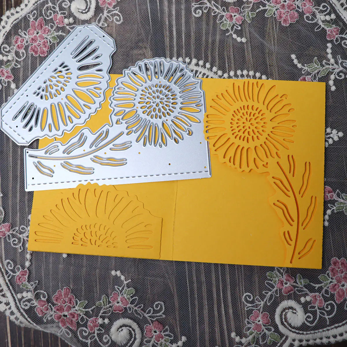 A yellow card adorned with a layered sunflower embellishment, accompanied by the Printable Heaven Large Sunflower Cutting Die (2 PCS) (B049), displayed on a lace tablecloth with a floral pattern.