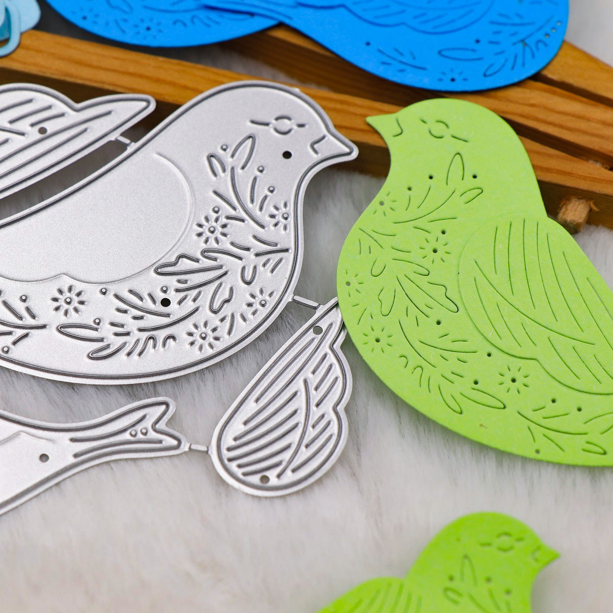 Here’s a rewritten version of the sentence, incorporating your product data: A close-up showcases the Printable Heaven Decorative Bird Cutting Die Set – 3D Wing Design (4 PCS) (SP126), featuring intricately etched metallic silver and green paper bird cutouts with striking three-dimensional wings. Additional blue bird shapes appear in the background, demonstrating the versatility of this advanced papercraft die set for creative projects.