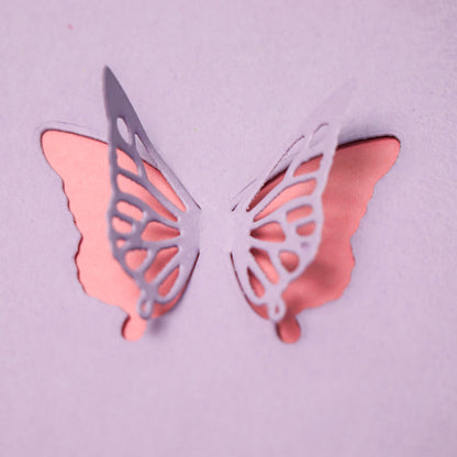 A butterfly cut from the Printable Heaven Delicate Butterfly Cutting Die (2 PCS) (A188) is partially raised from a pink surface, unveiling a deeper pink layer beneath—an ideal way to add beautiful dimension to your paper crafting creations.
