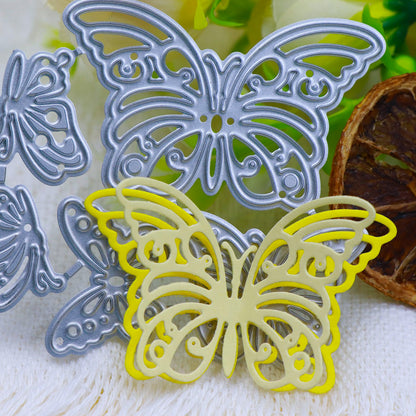 Metal and yellow paper butterfly-shaped cutouts, crafted with the Printable Heaven Fluttering Butterflies Cutting Die (5PCS) (A214), are beautifully arranged on a white textured surface, accented by green and white flowers and a dried brown slice in the background—ideal inspiration for your next cardmaking supplies collection.