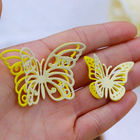 A hand holding two delicate, yellow, cut-out butterfly decorations—one larger and one smaller—with intricate wing designs, beautifully crafted using the Printable Heaven Fluttering Butterflies Cutting Die (5PCS) (A214), ideal for cardmaking supplies.