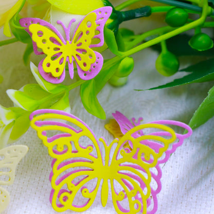Two decorative butterflies, yellow with pink edges, rest on lush green artificial leaves against a white textured background—perfect inspiration for your next project using the Fluttering Butterflies Cutting Die (5PCS) (A214) from Printable Heaven or other cardmaking supplies.