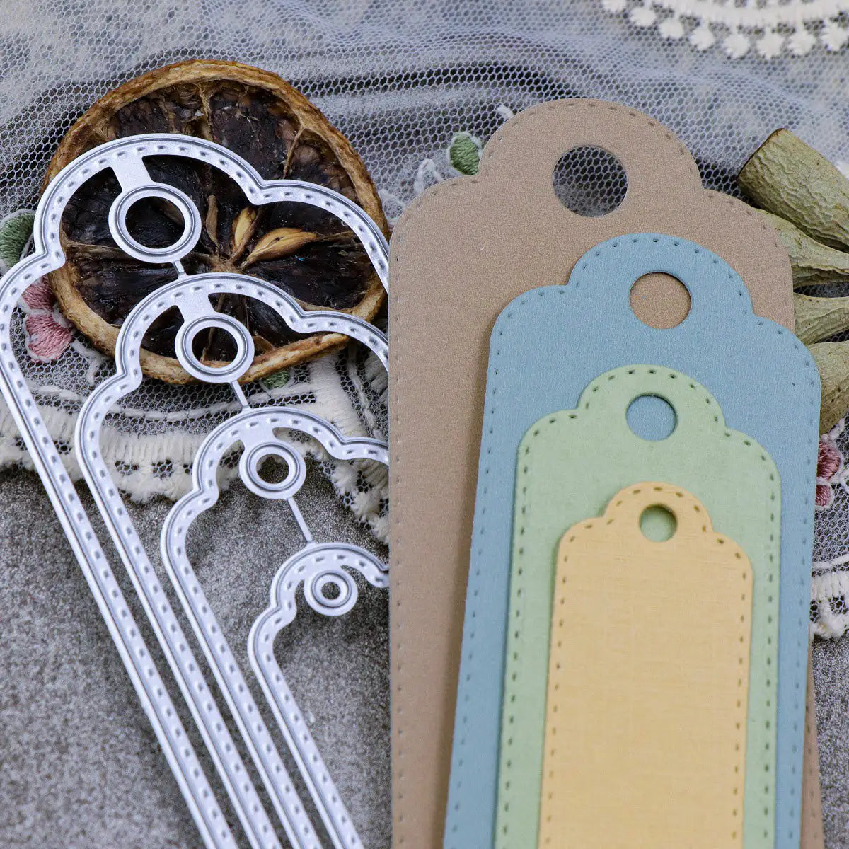 The Printable Heaven Stitched Edge Tags Die Set (4 PCS) (SP068) is displayed alongside vibrant paper tags in different sizes on a textured background featuring lace, dried citrus, and rustic accents—ideal inspiration for creative paper crafting projects with these versatile stitched edge tag dies.