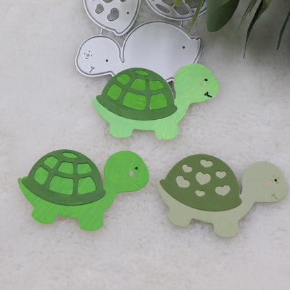 Featuring the Printable Heaven Turtle/Tortoise Cutting Die (3 PCS) (A203), this scene displays three charming turtle-shaped cutouts: two are vibrant green with classic shell patterns, and one is light green adorned with heart shapes on its shell. The metal cutting die is visible in the background along with leafy accents—making these delightful scrapbook embellishments ideal for card making and creative projects.