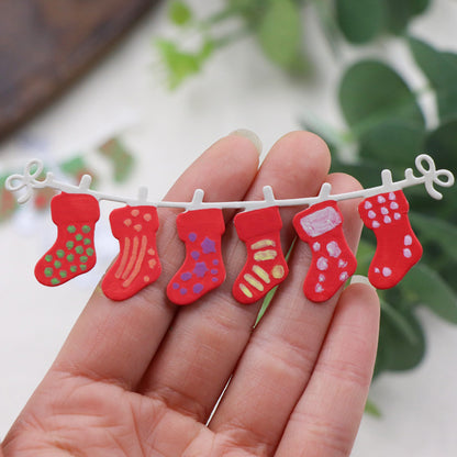 A hand displays the Printable Heaven Christmas Stocking Garland Cutting Die (1 PC) (SP050), featuring a miniature string of six red stockings with unique, colorful patterns—an adorable handmade decoration perfect for Christmas crafting.