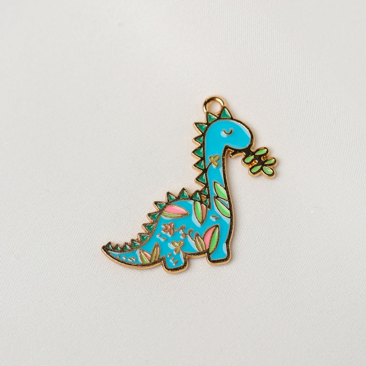 Printable Heaven Dinosaur Metal Charm (1pc) (MLB-072) shaped like a blue dinosaur with green and pink floral-style patterns holding a small leaf in its mouth.