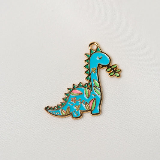 Printable Heaven Dinosaur Metal Charm (1pc) (MLB-072) shaped like a blue dinosaur with green and pink floral-style patterns holding a small leaf in its mouth.